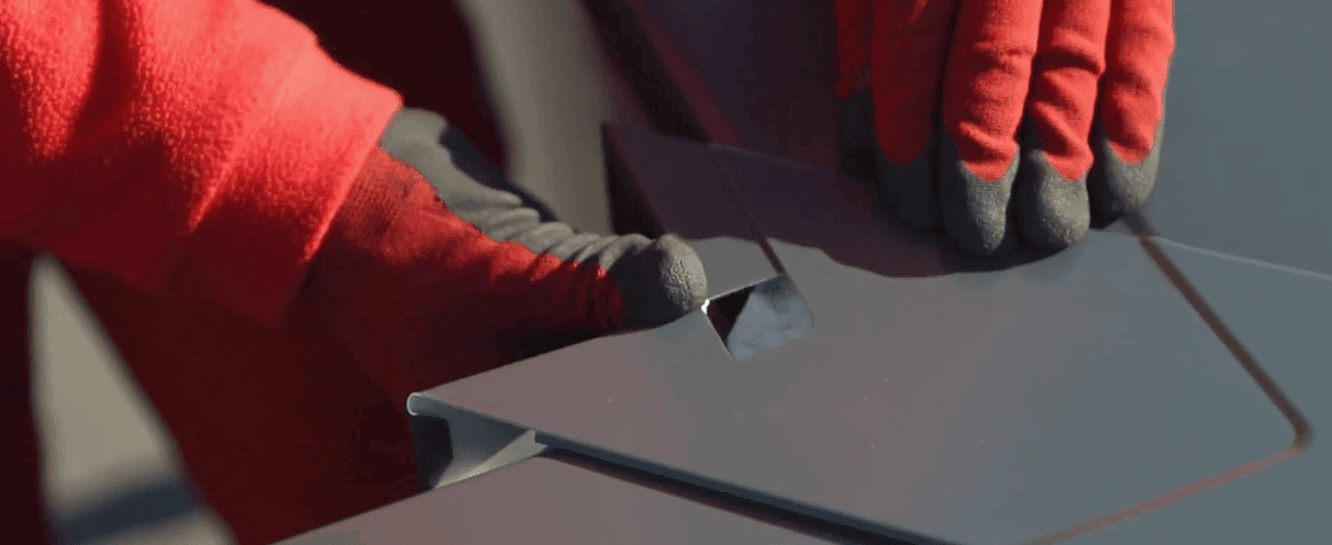Ouvrier manipulant une plaque en aluminium avec des gants rouges.