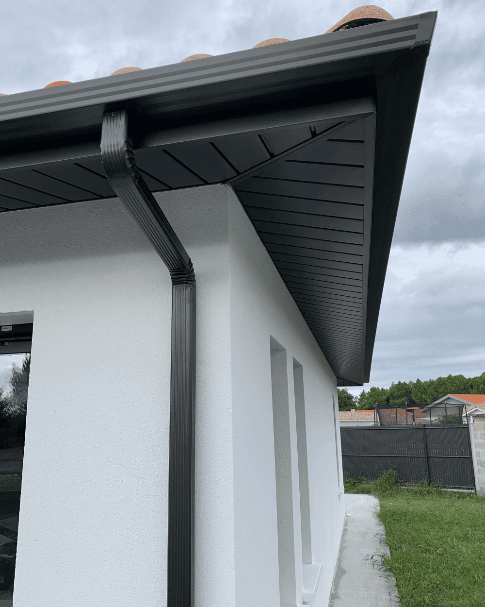 Gouttière noire et toiture en tuiles sur une maison moderne.